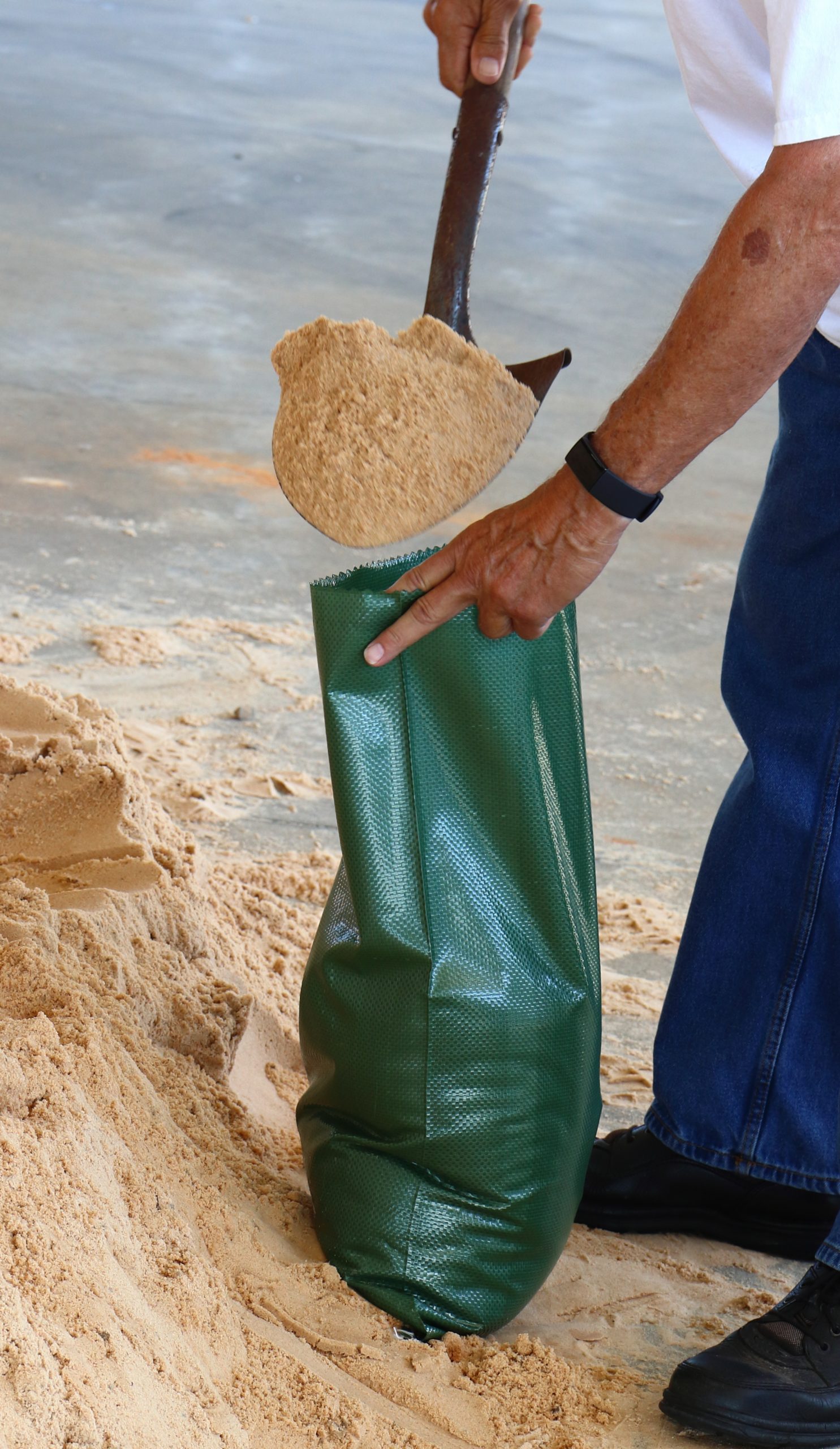 A person filling a sandbag with sand, preparing it for use to help protect property from potential flooding.