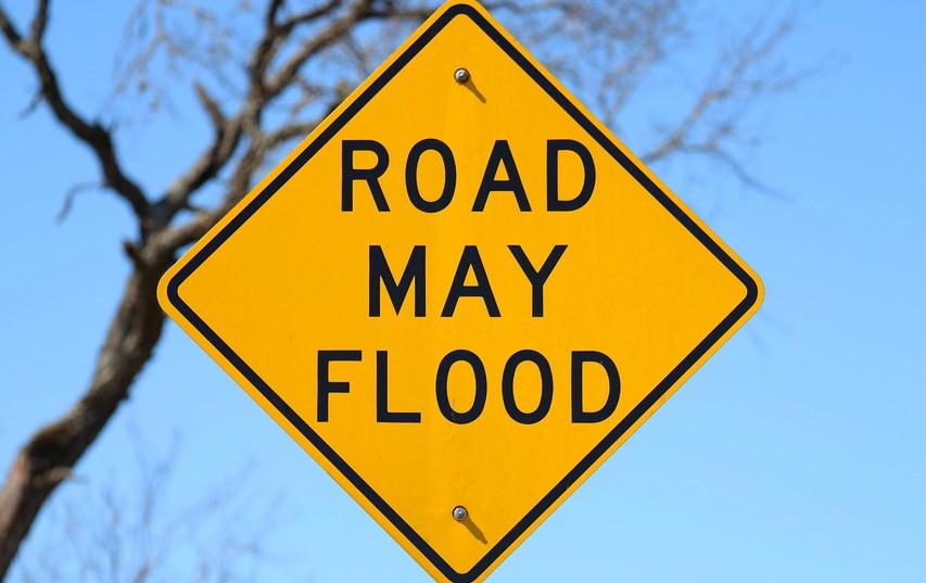 A yellow “Road May Flood” warning sign posted along a roadway to alert drivers of potential flooding hazards during heavy rain or high water conditions.